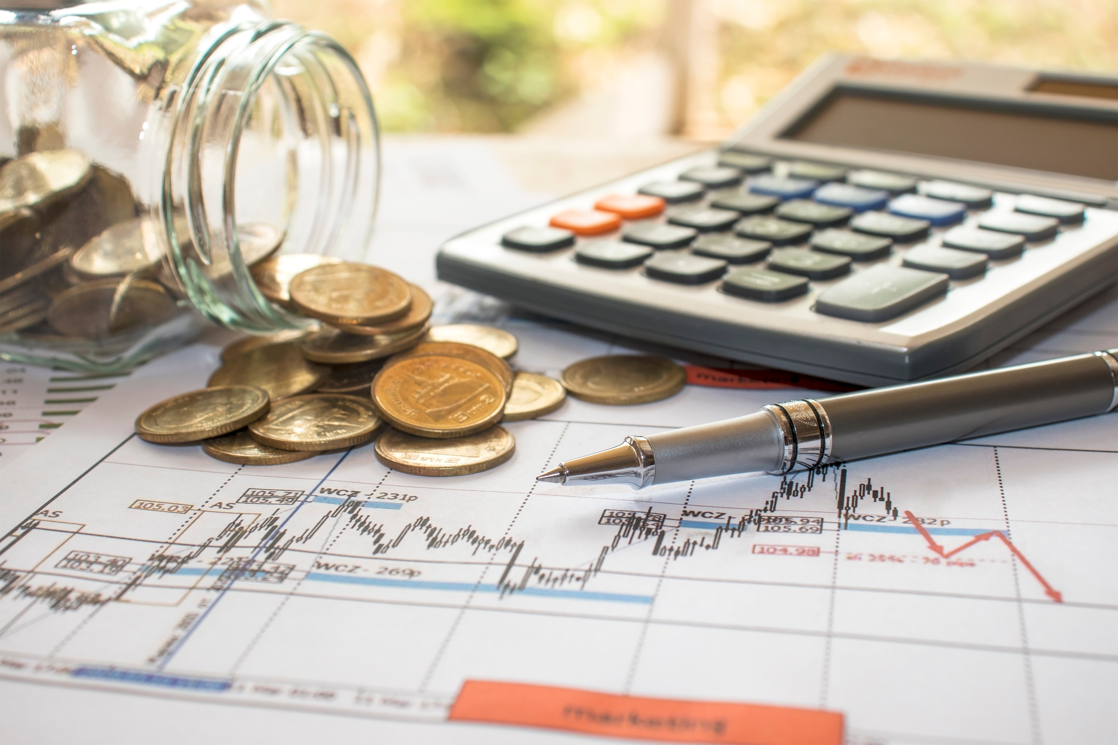 Pens and coins placed on financial reports or stock market chart analysis, placed on the table, financial income tax calculation concepts and financial monitoring concepts.