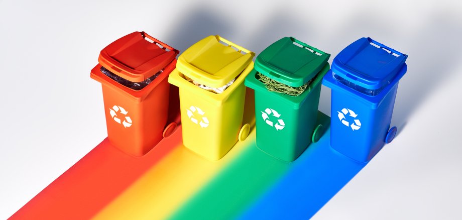 Four color coded recycle bins, isometric projection on geometric rainbow paper background with copy-space. Recycling sign on the bins - red, blue, yellow, green. Waste separation concept background.