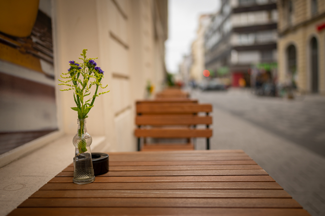 Single glass vase of purple statice and goldenrod flowers on wooden Vienna cafe table